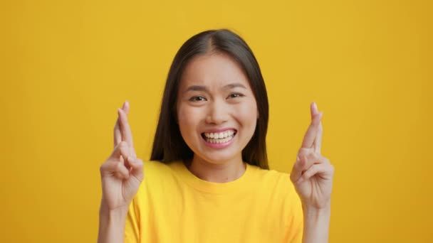 Ásia senhora cruzando dedos pedindo sorte sobre fundo amarelo — Vídeo de Stock