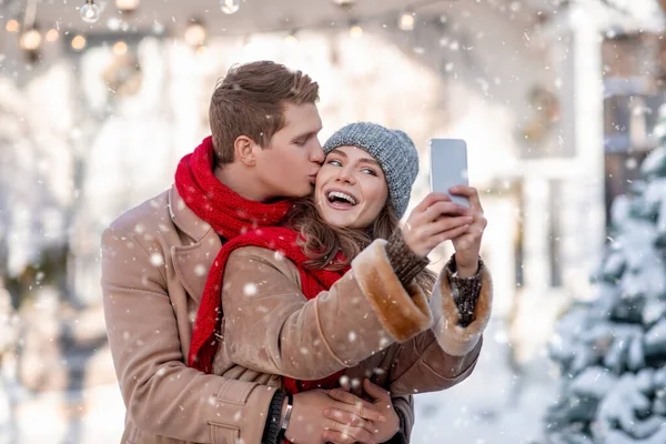 Pareja alegre disfrutando de la primera nieve, tomando selfie juntos —  Fotos de Stock