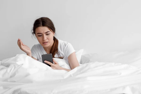 Збентежена дівчина з Європи, яка переживає горе, отримує погане повідомлення, сидить на білому ліжку у спальні. — стокове фото