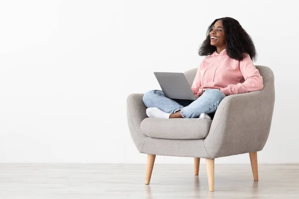 Mujer afroamericana positiva sentada en sillón con portátil —  Fotos de Stock