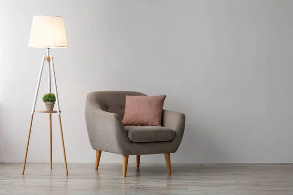 Wygodny fotel z różową poduszką, świecąca lampa na podłodze na szarym tle ściany w biurze lub salonie — Zdjęcie stockowe