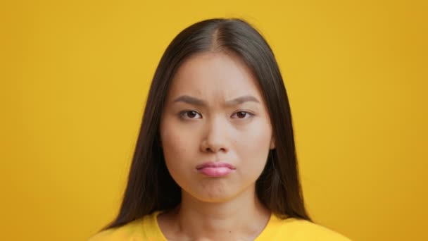 Unzufriedene Japanerin blickt auf Kamera, die vor gelbem Hintergrund posiert — Stockvideo