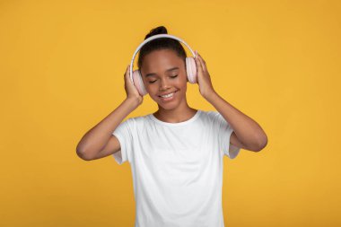 Beyaz tişörtlü, kulaklıklı, müzik dinleyen Afro-Amerikan kız.