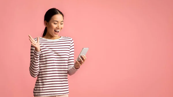 Überraschte junge Asiatin schaut aufs Smartphone und ruft begeistert — Stockfoto