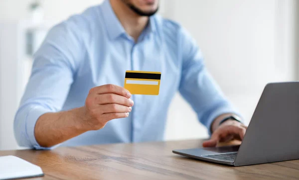 Nierozpoznawalny Arab z laptopem i kartą kredytową kupujący towary przez internet w biurze, zbliżenie — Zdjęcie stockowe