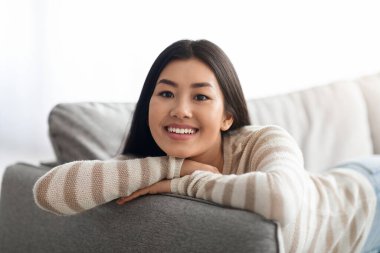 Ev içi rahatlık. Gülümseyen Koreli Kadın Oturma odasında dinleniyor