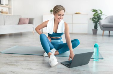 Gülen kadın yoga minderinde dizüstü bilgisayar kullanarak oturuyor.