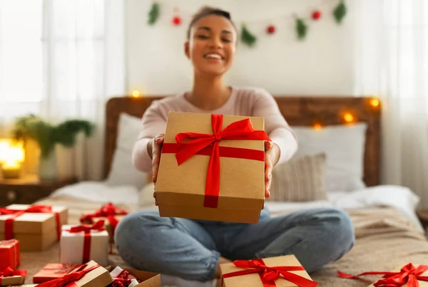 겨울 연휴 개념. 해피 아프리카계 미국 여성 크리스마스 선물 상자를 카메라로 늘여 침대에 앉아 — 스톡 사진