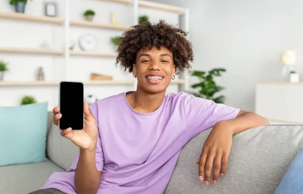 Vrolijke Afro-Amerikaanse tiener kerel toont mobiele telefoon met leeg scherm thuis, mockup voor mobiele app of website — Stockfoto