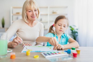 Büyükanne ve torun evde boyayla resim çiziyor.