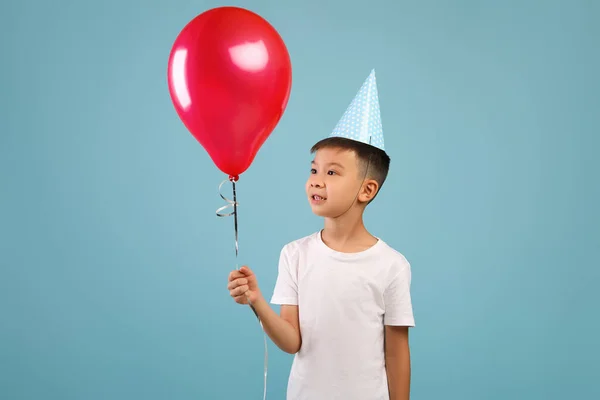 Šťastný malý asijský B-Day Boy nosící Party klobouk drží červený balón — Stock fotografie