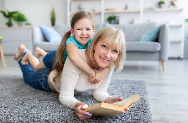 Feliz mujer madura y nieta leyendo libro en casa —  Fotos de Stock