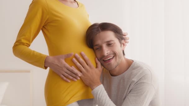 拍下幸福的未来爸爸的肖像，听着他怀孕的妻子的肚子，微笑着，享受着婴儿的隆隆声 — 图库视频影像