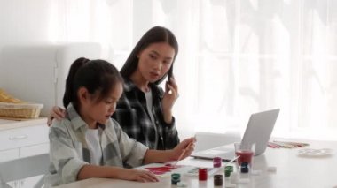 Asyalı anne cep telefonuyla konuşuyor. Kucaklayan kız evde çalışıyor.