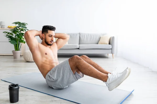 Longitud completa del hombre árabe en forma fortaleciendo los músculos del núcleo, haciendo ejercicios abdominales en la esterilla en casa — Foto de Stock