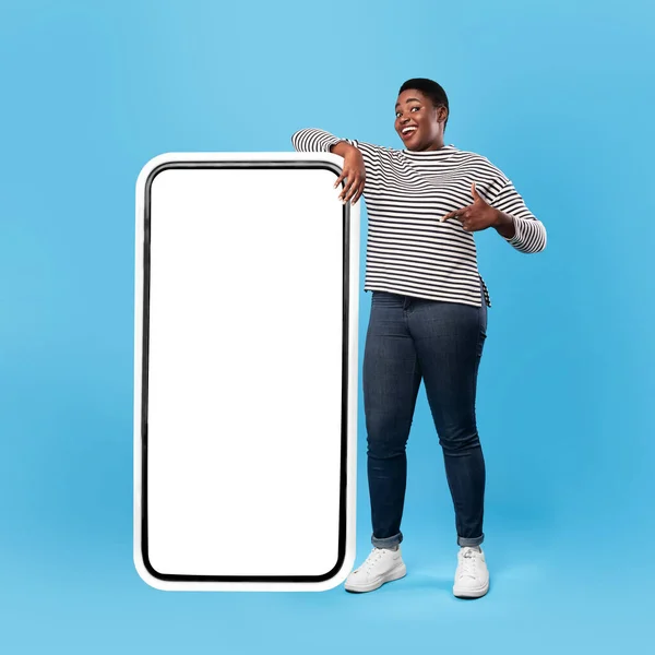蓝色背景，站在巨型智能手机附近的黑色女性显示屏 — 图库照片