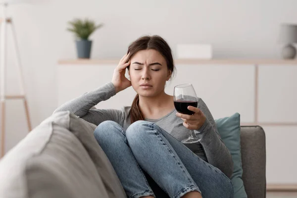 Сумна байдужа кавказька молода леді сидить на дивані з келихом вина і страждає від головного болю вдома — стокове фото