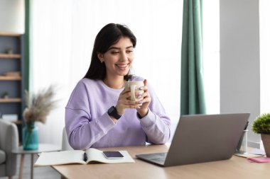 Mutlu bayan video izliyor, elinde fincanla kahve içiyor.