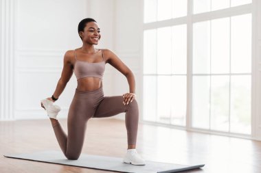 Happy young black woman stretching leg exercising on yoga mat clipart