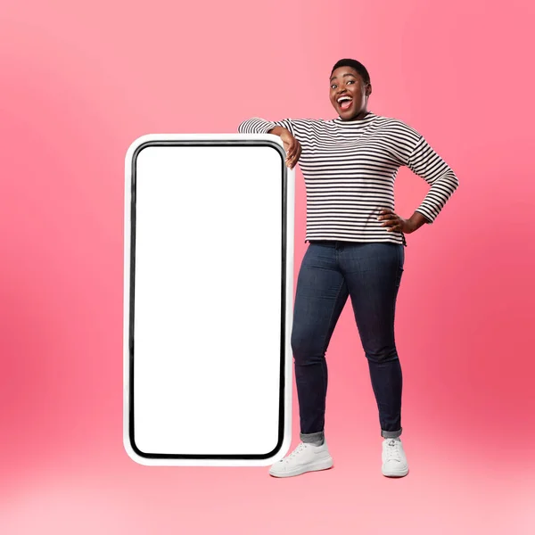 Femme afro-américaine debout près du grand écran de téléphone, fond rose — Photo