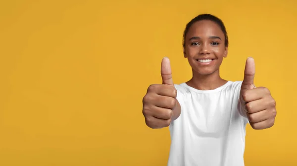 Fröhliche afroamerikanische Schülerin im weißen T-Shirt jubelt über den Erfolg und zeigt Daumen hoch, Nahaufnahme — Stockfoto