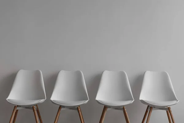 Wiersz czterech białych krzeseł na szarym tle ściany w biurze lub salonie — Zdjęcie stockowe