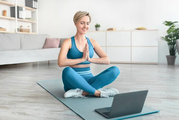 Woman meditating sitting in lotus position on mat with laptop — Stock Photo, Image