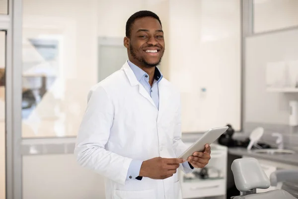 Diş Hizmetleri. Klinikte poz veren dijital tabletli yakışıklı siyah erkek dişçi — Stok fotoğraf