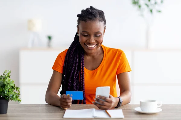 Positiv svart dam med modern mobiltelefon och kreditkort, betala för varor och tjänster på webben hemifrån — Stockfoto
