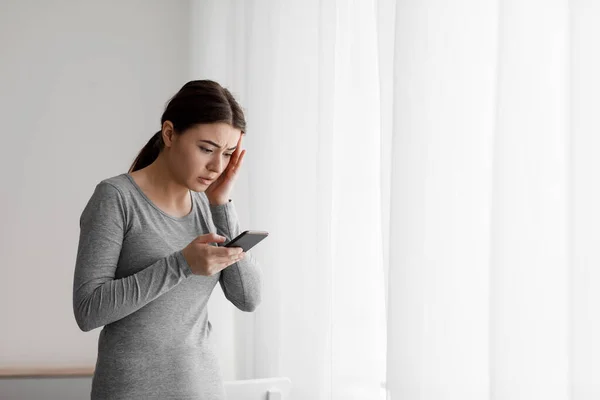 Verdrietig wanhopige jonge Europese dame ontvangt slecht nieuws op smartphone thuis — Stockfoto