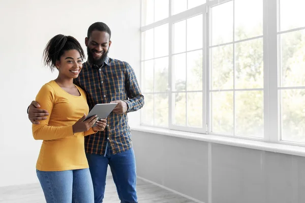 Sorrindo jovem afro-americano marido e mulher olhando em tablet, escolhendo interior para casa — Fotografia de Stock