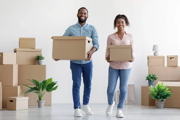 Alegre jovem afro-americano marido e mulher carregam caixas de papelão na sala de estar interior em nova casa — Fotografia de Stock