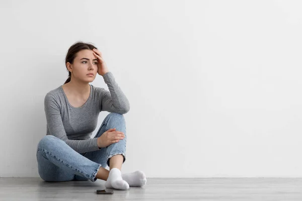 Sfrustrowana smutna, zmartwiona młoda kobieta czeka na telefon i myśli, siedzi na podłodze w domu — Zdjęcie stockowe