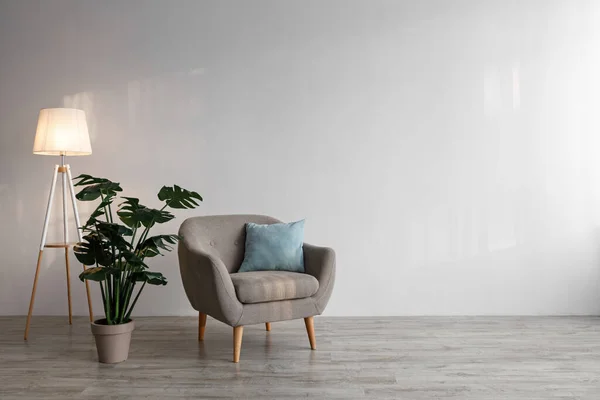 Przytulny fotel z poduszką, świecąca lampa, duża zielona roślina w garnku na podłodze na szarym tle ściany — Zdjęcie stockowe