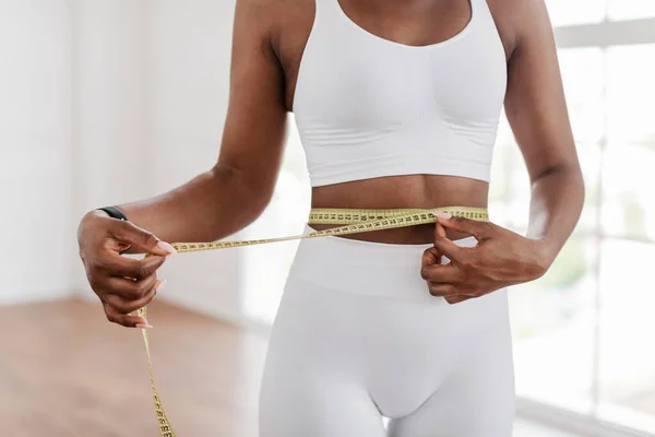 Черная женщина измеряет талию лентой. Концепция похудения — стоковое фото
