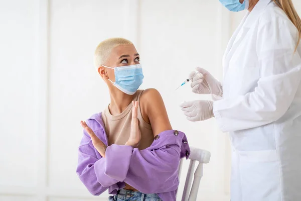 Mujer joven asustada de hacer la inyección de la vacuna contra el coronavirus, haciendo el gesto STOP, oponiéndose a la inmunización contra el covid-19 — Foto de Stock