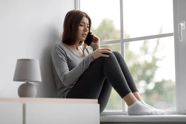 Sedih tertekan eropa milenial wanita duduk di jendela berbicara di telepon, mendapatkan kabar buruk — Stok Foto