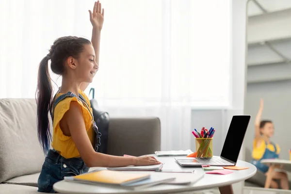 Menina sentada à mesa, usando laptop, levantando a mão para resposta — Fotografia de Stock
