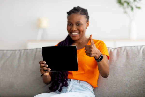 Positiv afro kvinna visar tablett med mockup för shopping app eller hemsida, visar tummen upp hemma, selektivt fokus — Stockfoto