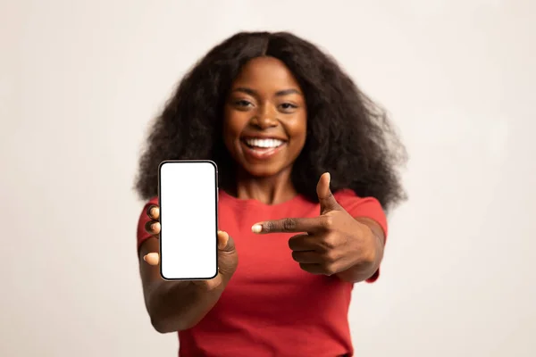 Мобильное приложение. Веселая черная женщина указывает на смартфон с чистым белым экраном — стоковое фото