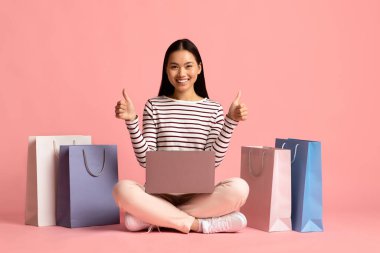 Alışveriş poşetlerinin arasında dizüstü bilgisayarla oturan Mutlu Asyalı Kadın