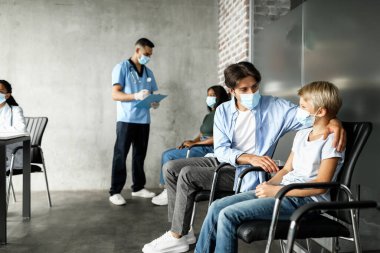 Babası oğlunu teselli ediyor, klinikte birlikte aşı olmayı bekliyor.