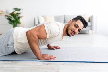 Milenyum Arap erkeği yoga minderinde durup, evde güç egzersizleri yapıyor.
