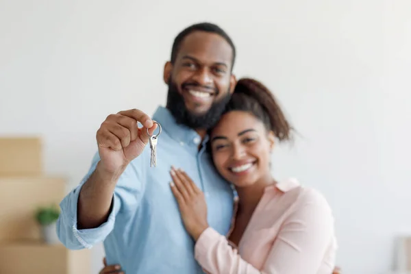 Cheerful young african american husband hugs wife and shows keys in room with cardboard boxes — Stock Photo, Image