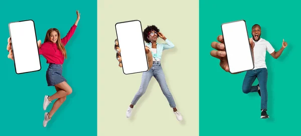 Alegre adolescente y millennial caucásico y negro hombre y mujeres se divierten, saltando y mostrar teléfonos inteligentes con pantalla en blanco — Foto de Stock