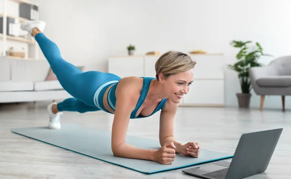 Gelukkig vrouw doen plank met been verhogen met behulp van laptop — Stockfoto