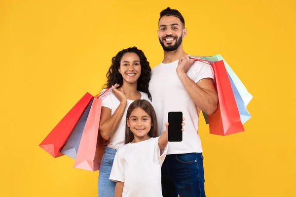 Familia de Oriente Medio Mostrando Smartphone posando con bolsas de compras, fondo amarillo —  Fotos de Stock