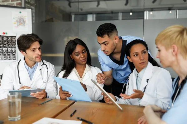 Equipo multiétnico concentrado de médicos sentados en la mesa, conversando —  Fotos de Stock