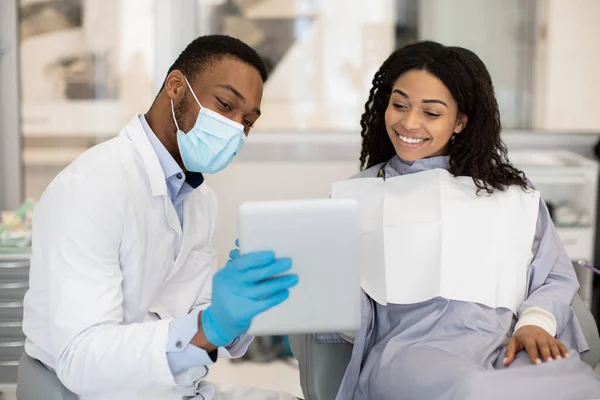Médico dentista discutiendo tratamiento con paciente femenina, mostrando resultado en tableta digital — Foto de Stock