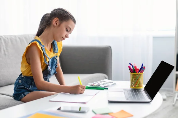 Menina sentada na mesa, usando laptop, escrevendo no livro — Fotografia de Stock